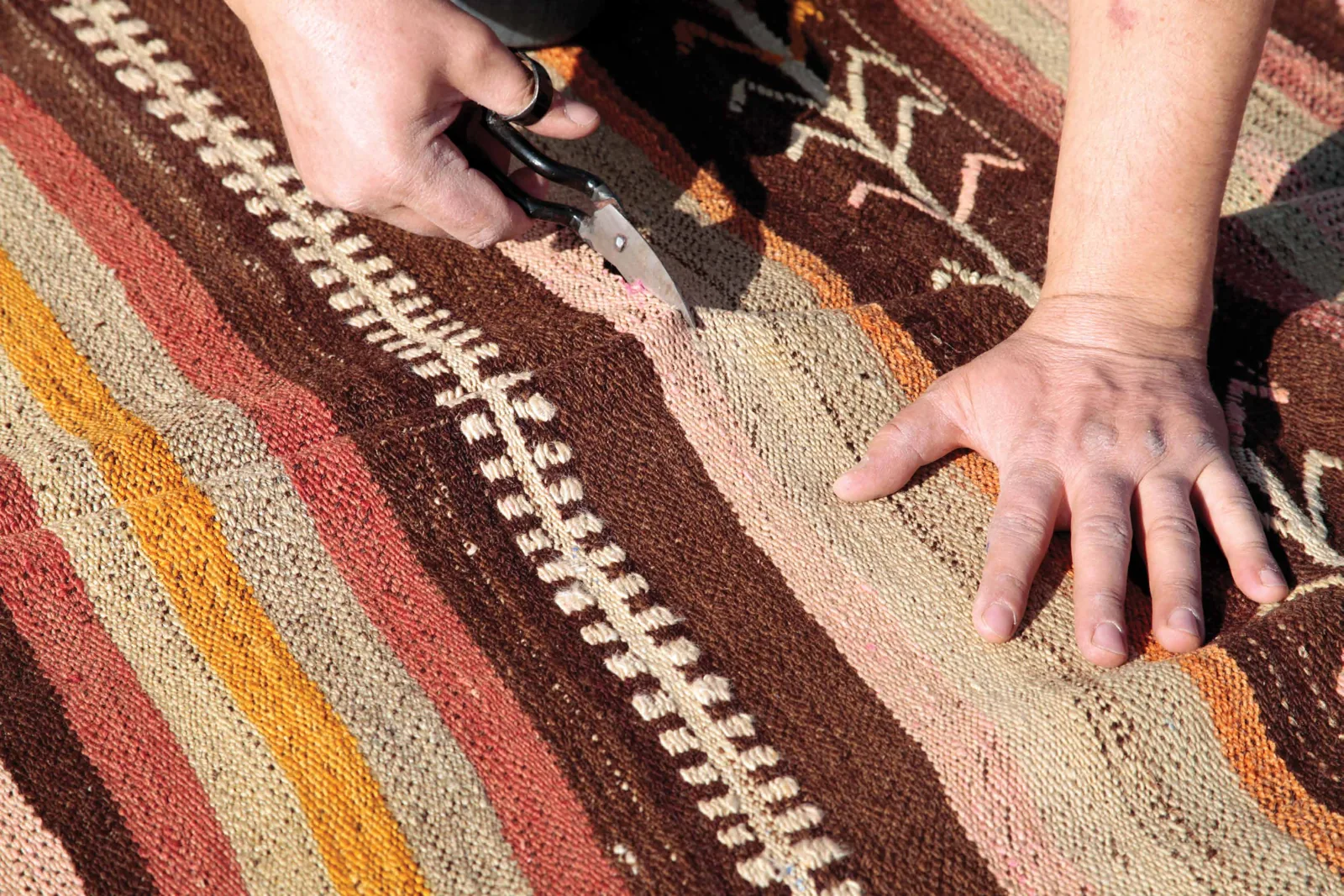 Hands carefully finishing the surface of a patterned carpet